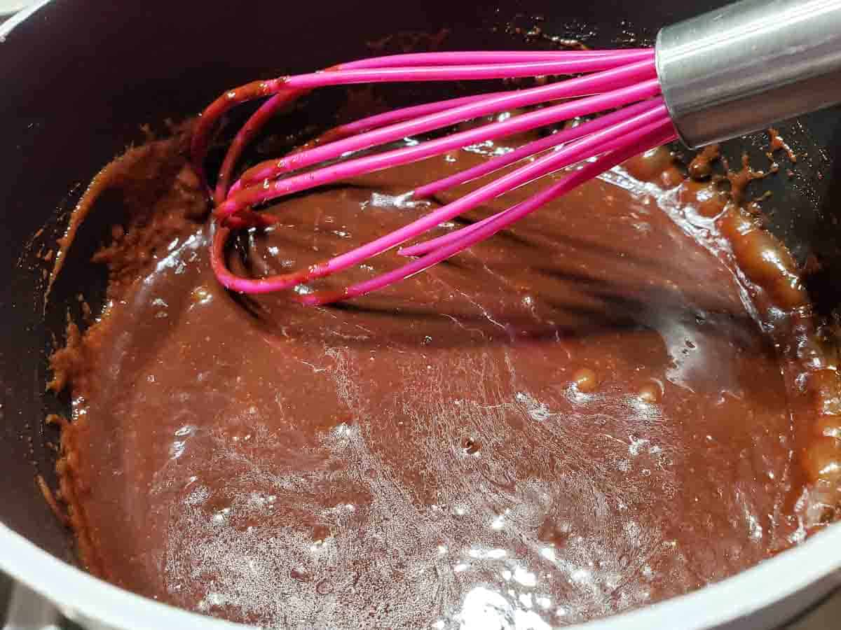 butter, sugar, milk, and cocoa whisked and cooking in a sauce pan.