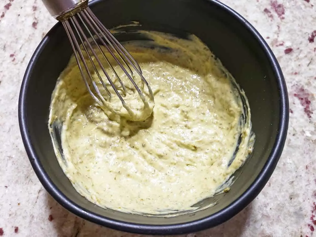 a bowl filled with creamy pesto mayo and a whisk.