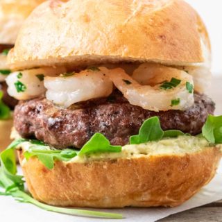 a surf n turf burger with beef patty, shrimp, arugula, and creamy pesto mayo.