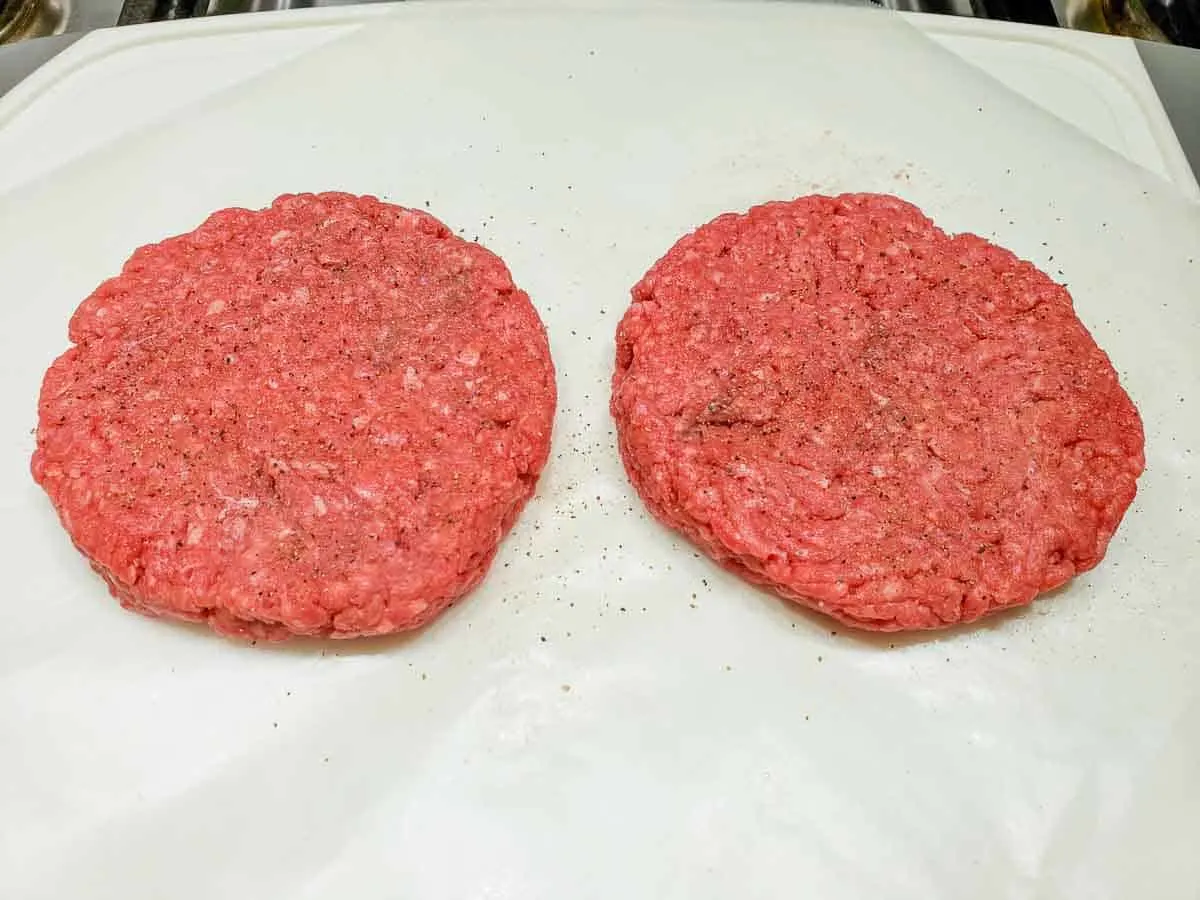 two ground sirloin beef patties sprinkled with salt and pepper.