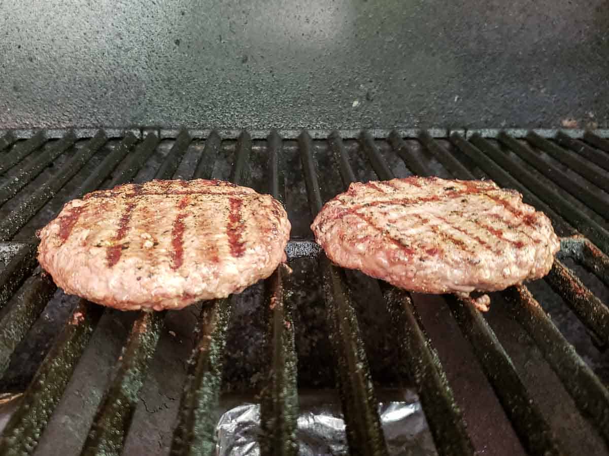 two ground sirloin burgers cooking on a grill.