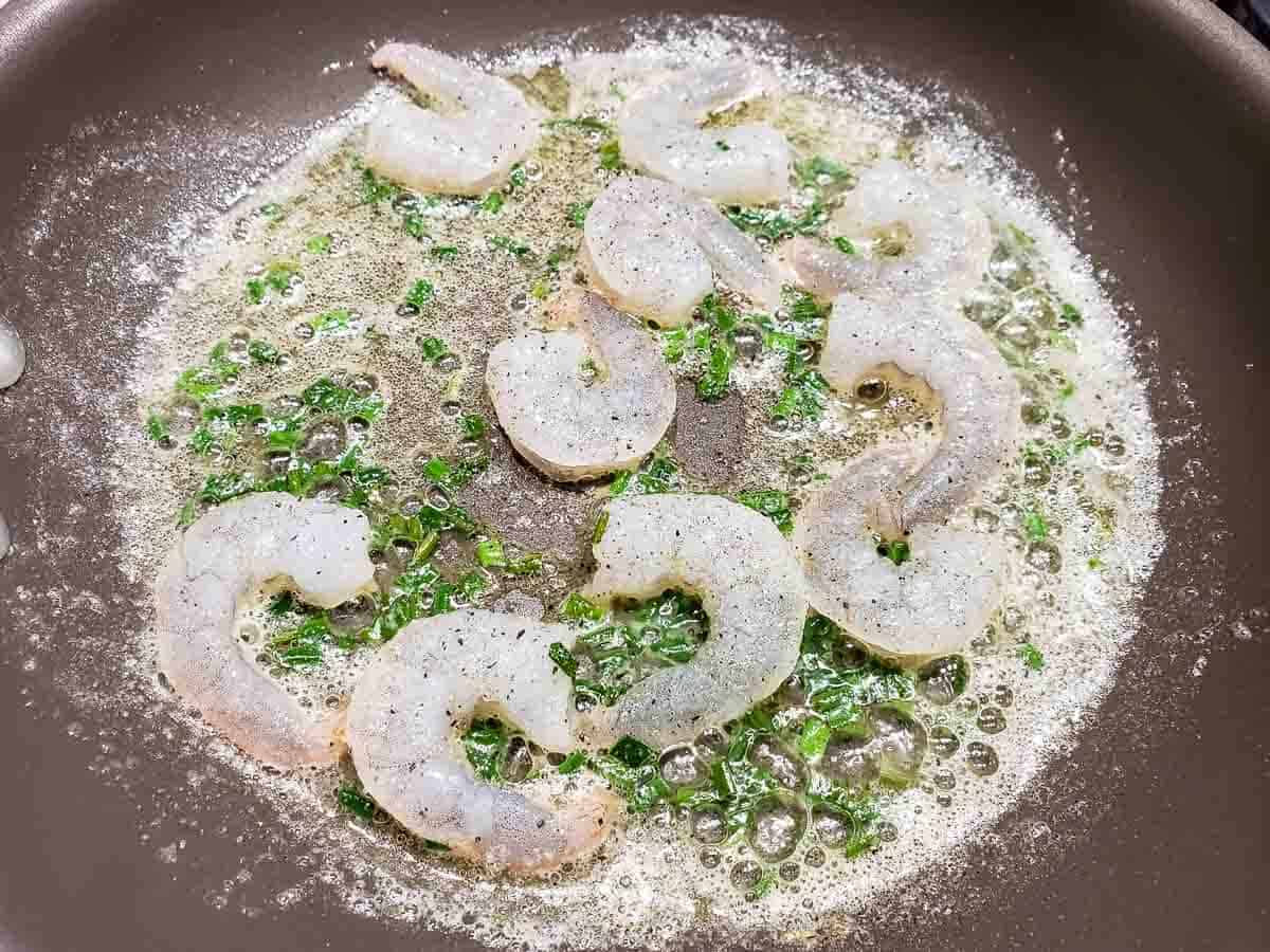 a frying pan filled with butter, fresh chopped chives, and raw shrimp.