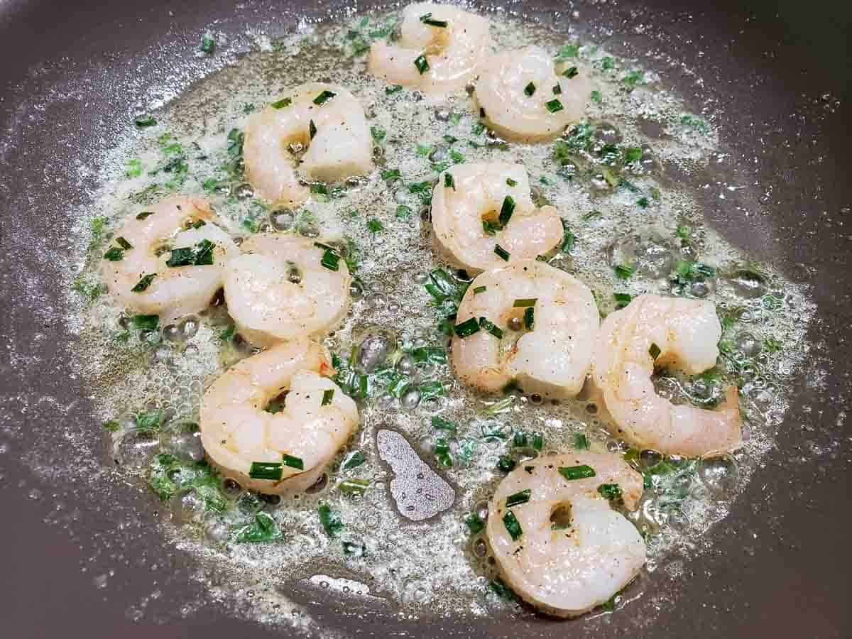 a frying pan filled with butter, fresh chopped chives, and pink shrimp.