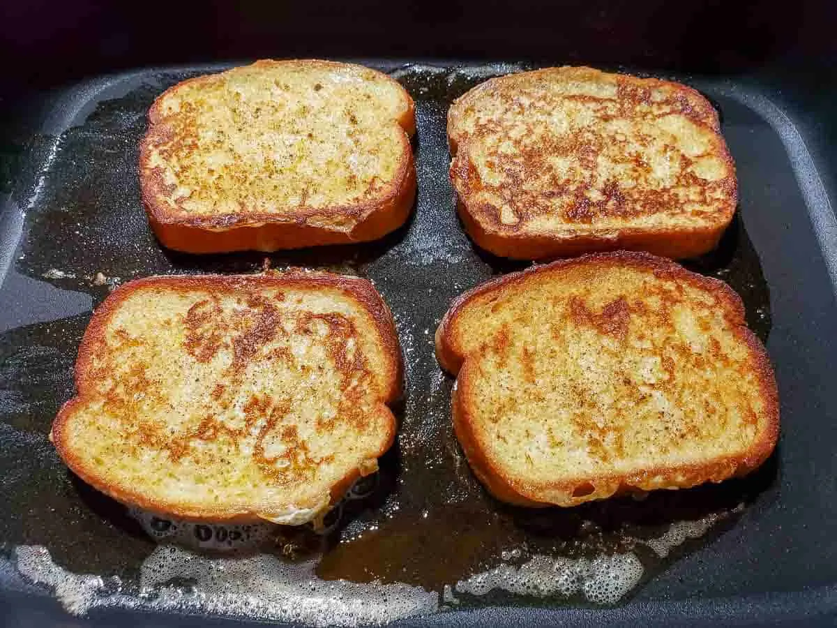 four slices of texas toast french toast frying in an electric skillet.