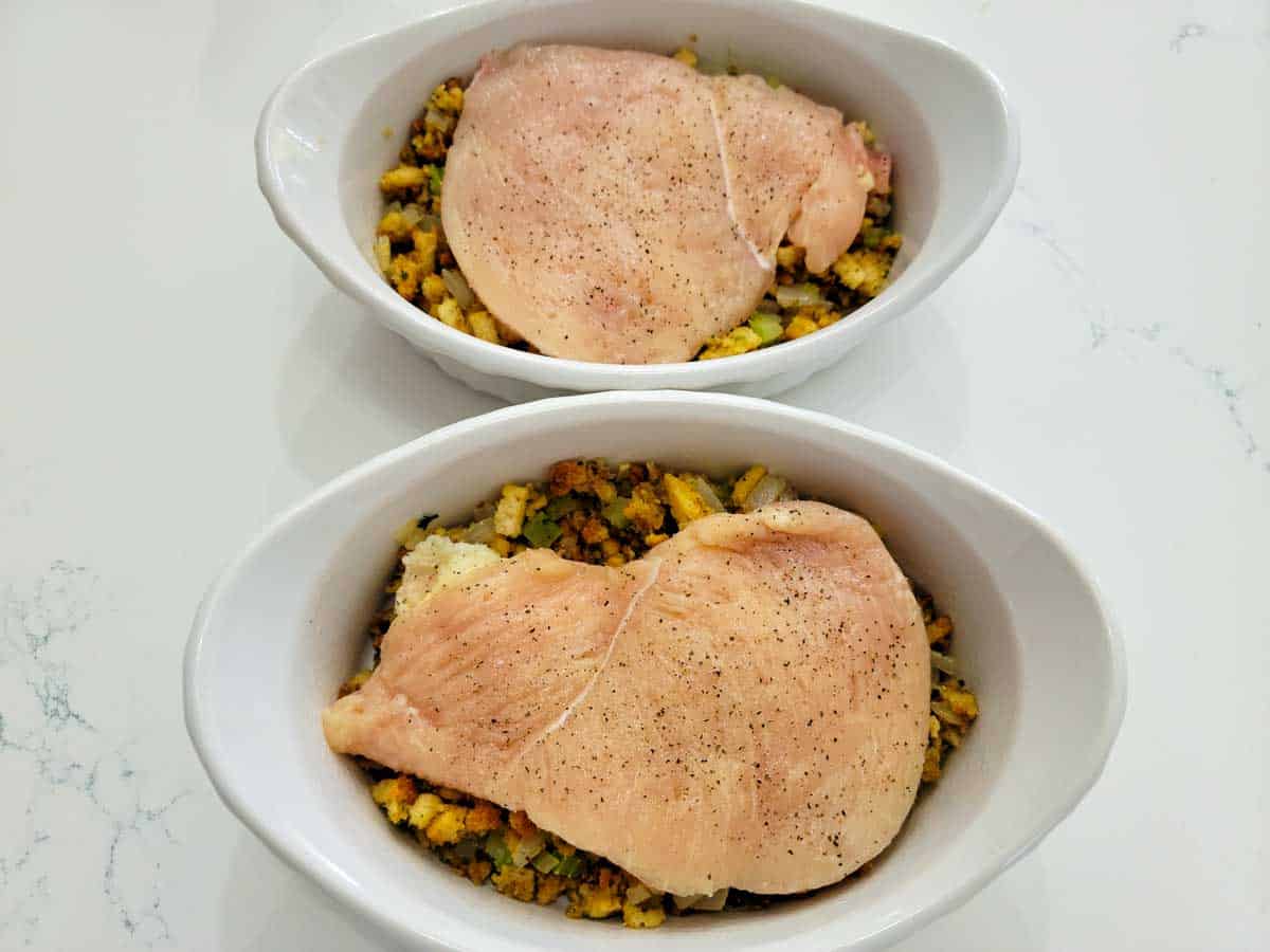 two baking dishes filled with homemade stuffing topped with boneless chicken.