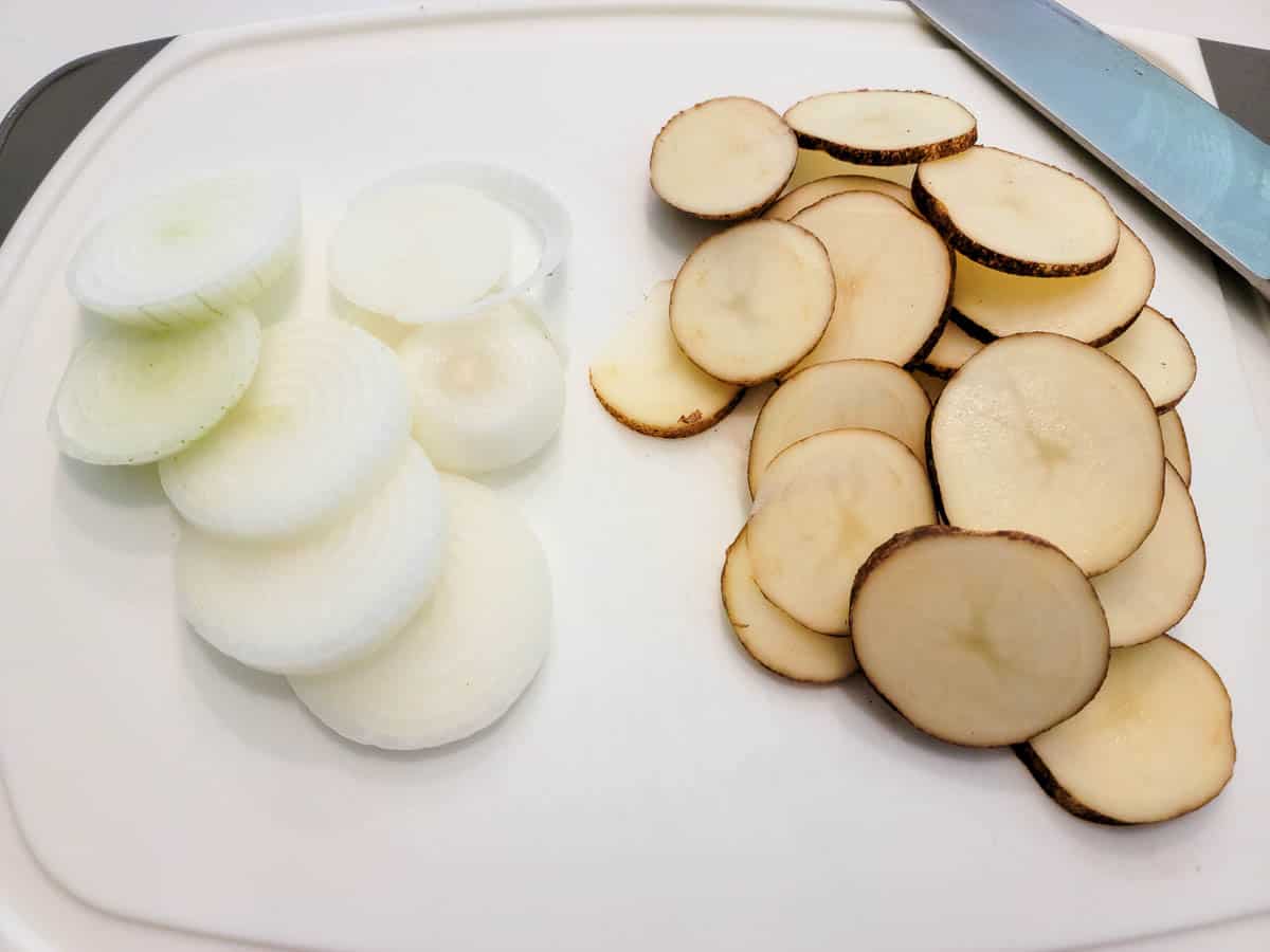 sliced onions and potatoes on a cutting board.
