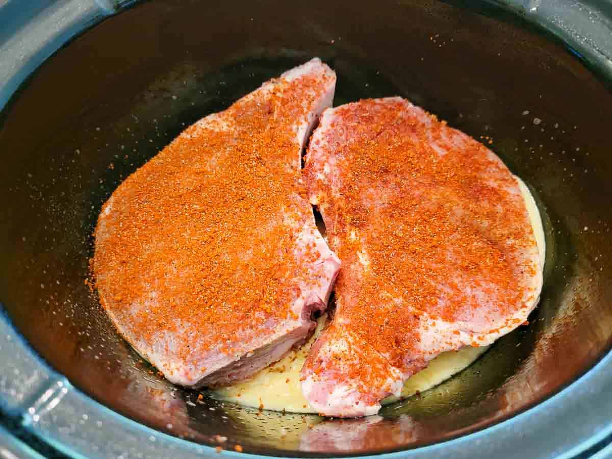 two pork chops covered in dry rub seasonings added to a slow cooker.