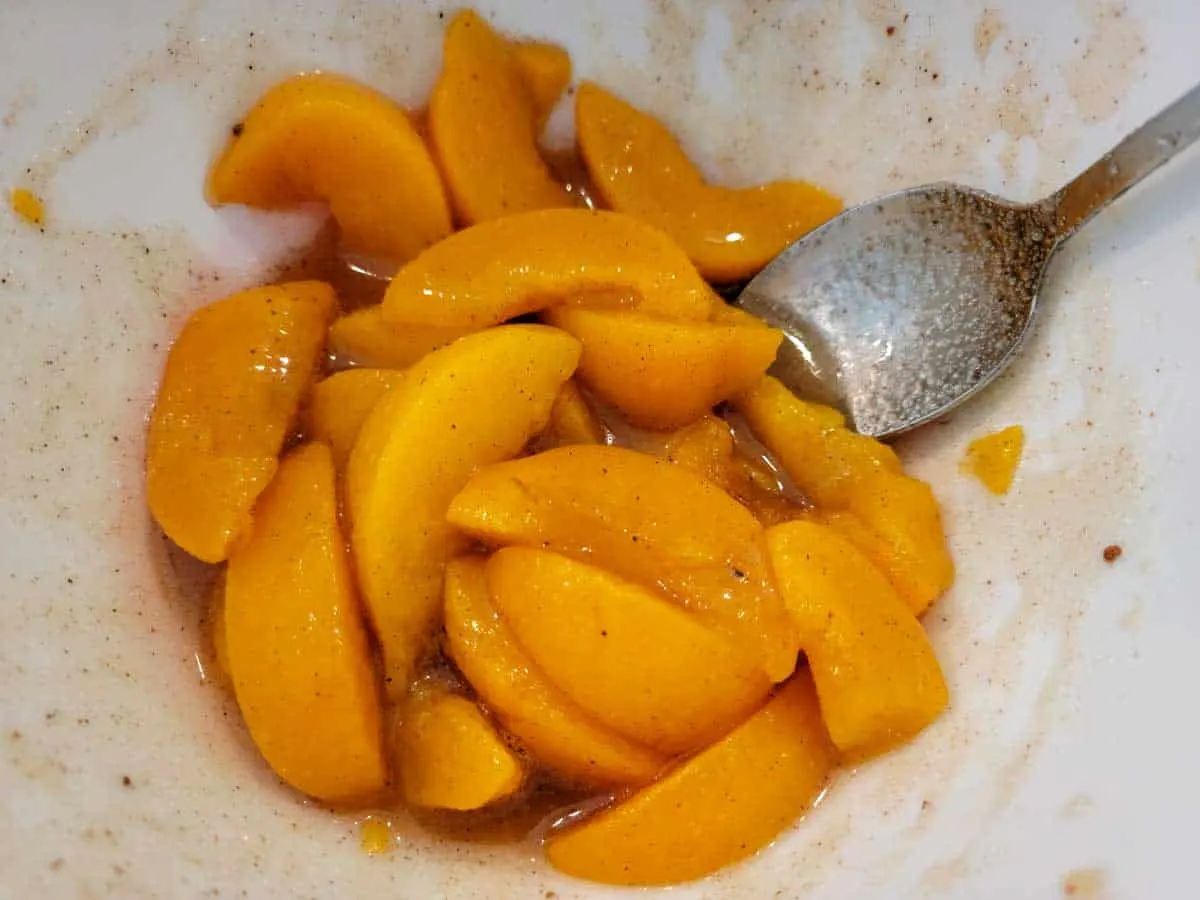 a bowl filled with slice peaches, cinnamon, and nutmeg.
