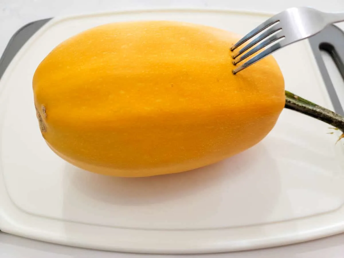 a fork poking holes in a spaghetti squash.