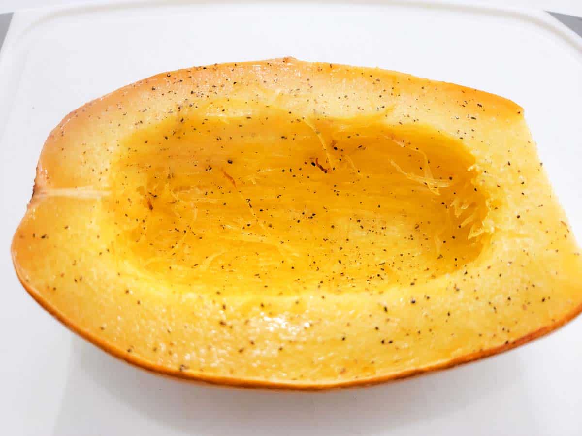 a baked spaghetti squash half cooling on a cutting board.