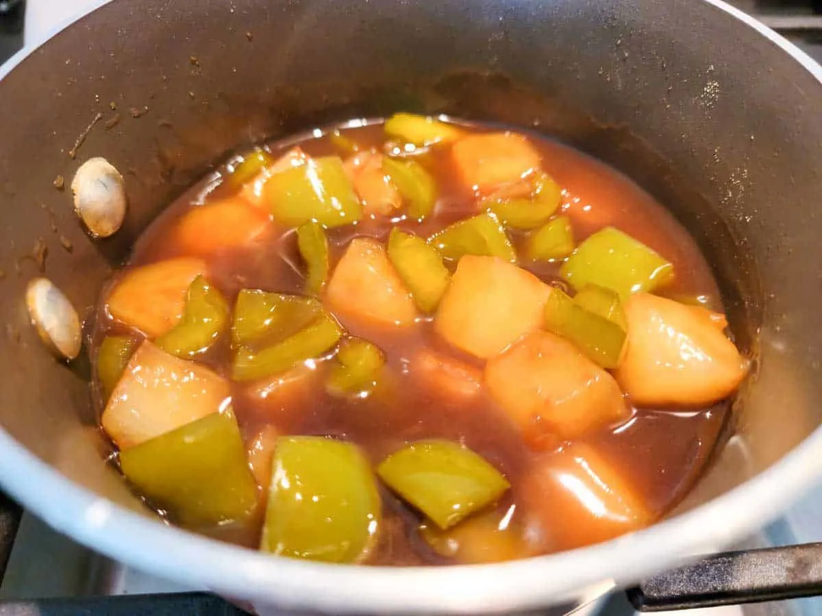 a sauce pan filled with pineapples, green peppers and brown sauce with cornstarch slurry stirred in.