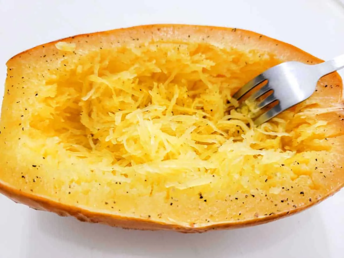 a fork raking spaghetti squash strands inside the shell.