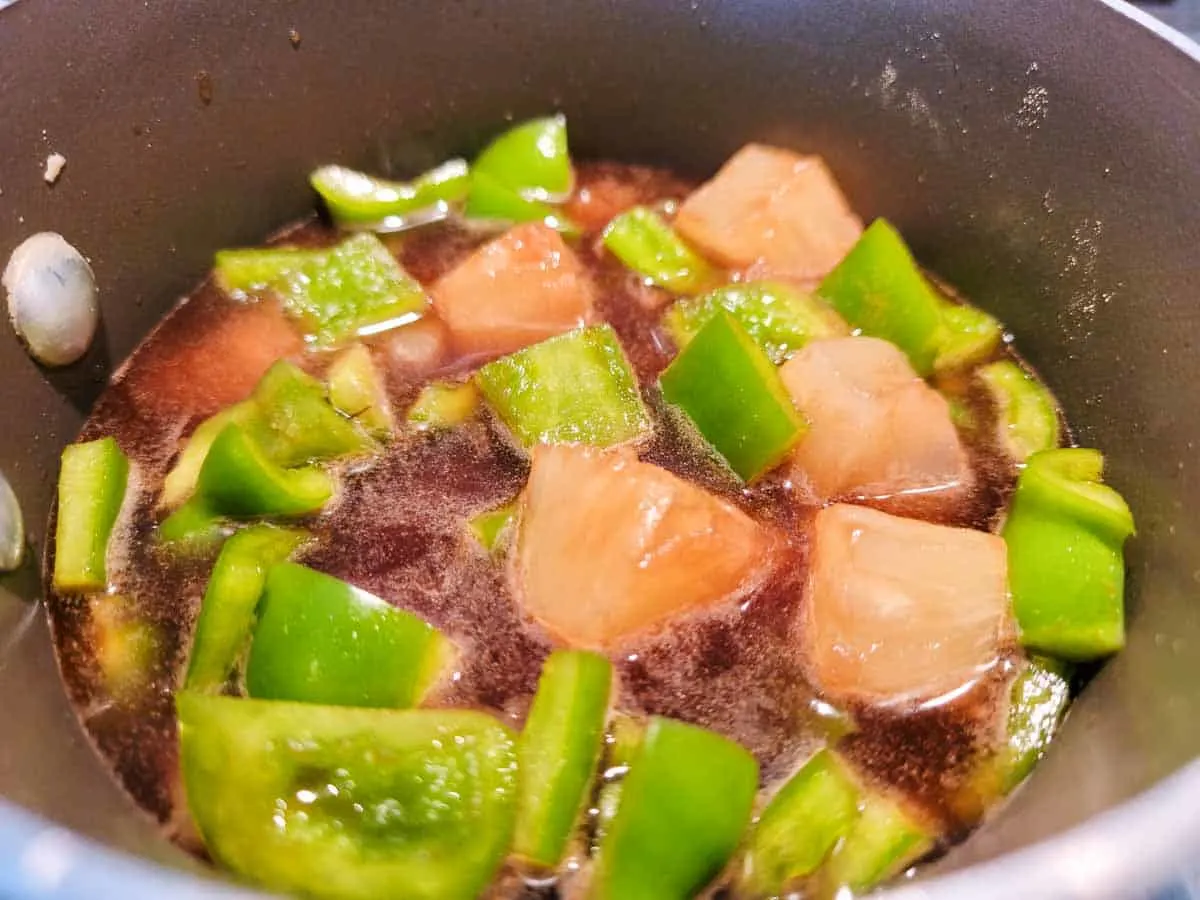 a sauce pan filled with pineapples, green peppers and brown sauce.