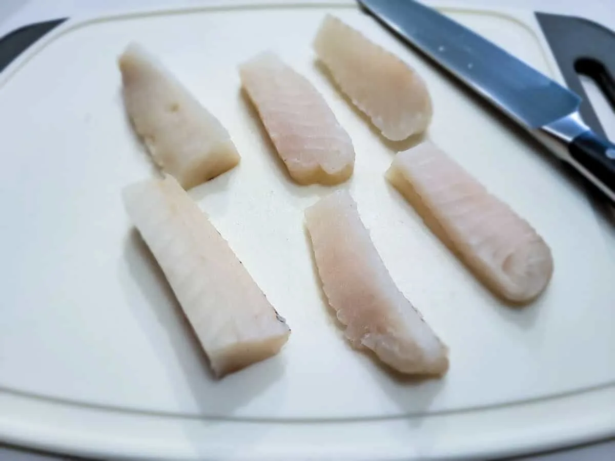 6 strips of cod on a cutting board.