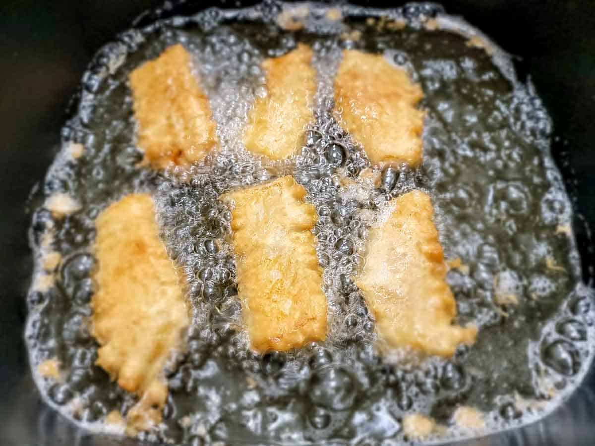 6 beer battered cod filets frying in an electric skillet.