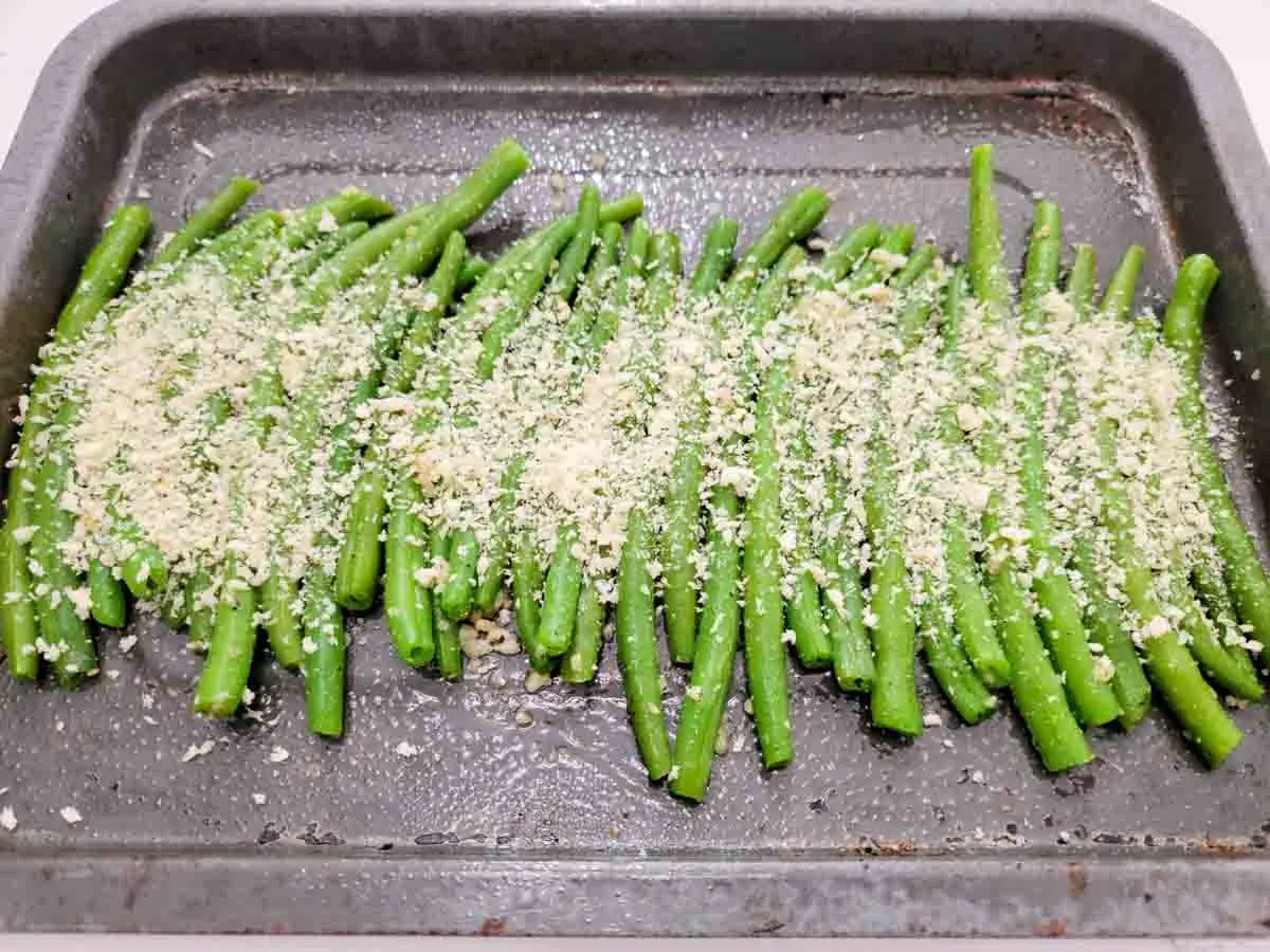 green beans in a row topped with panko bread crumbs on a baking sheet.