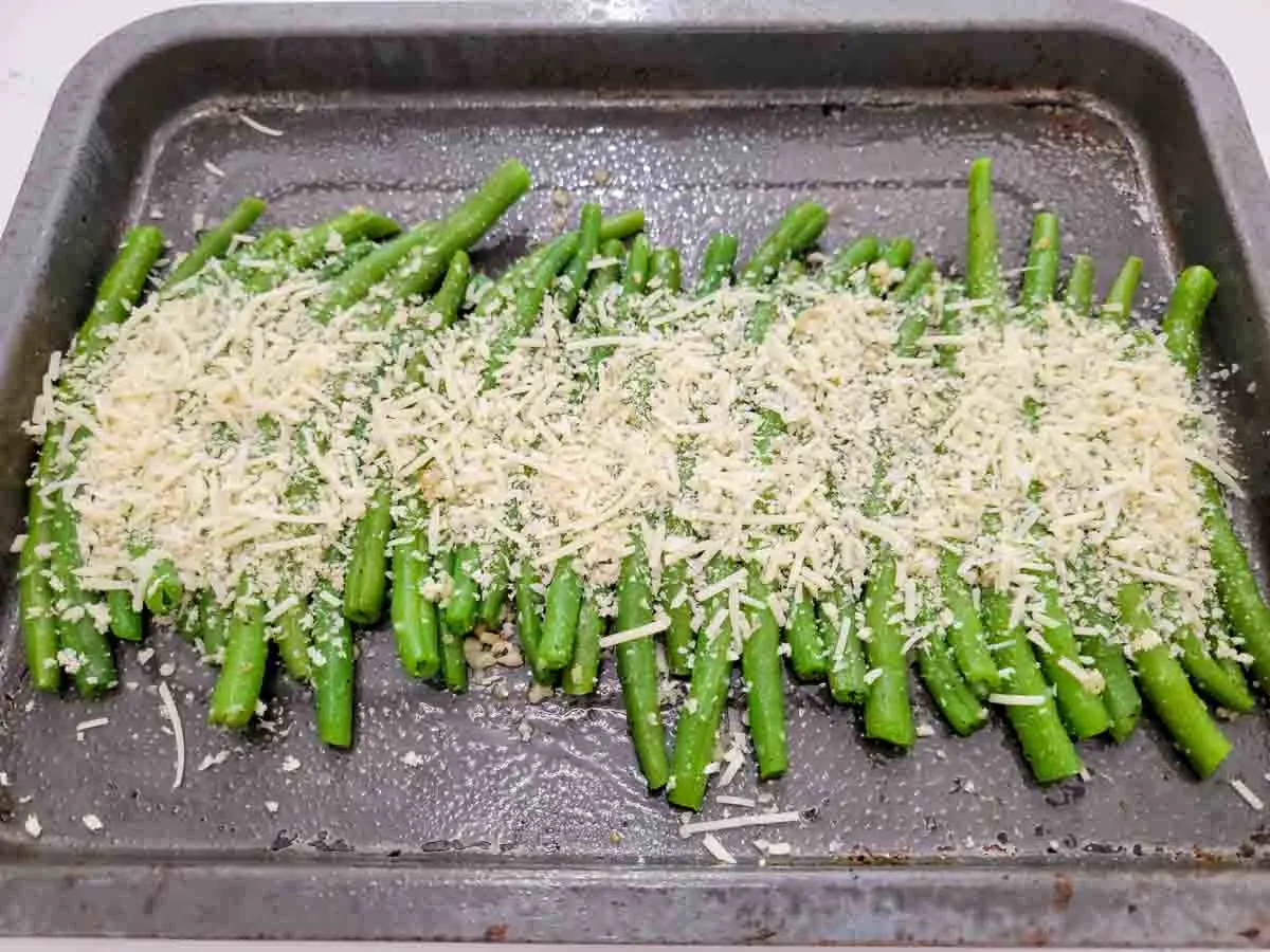 green beans in a row topped with panko bread crumbs and parmesan cheese on a baking sheet.