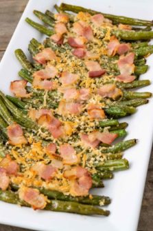 Baked green beans topped with parmesan cheese and bacon on a plate.