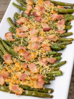 Baked green beans topped with parmesan cheese and bacon on a plate.
