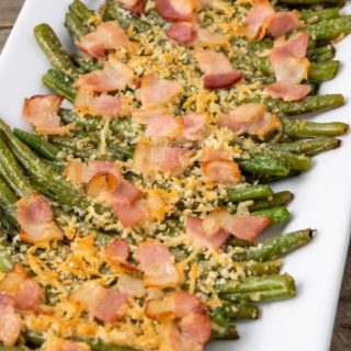 Baked green beans topped with parmesan cheese and bacon on a plate.