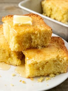 3 slices of cornbread topped with butter and honey on a plate and one slice left in the pan.