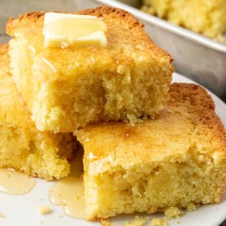 3 slices of cornbread topped with butter and honey on a plate and one slice left in the pan.