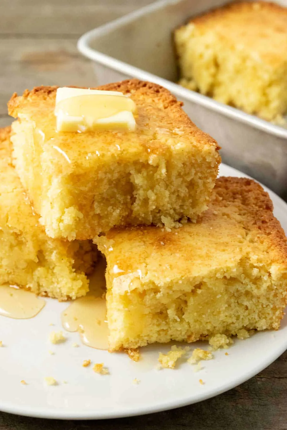 3 slices of cornbread topped with butter and honey on a plate and one slice left in the pan.