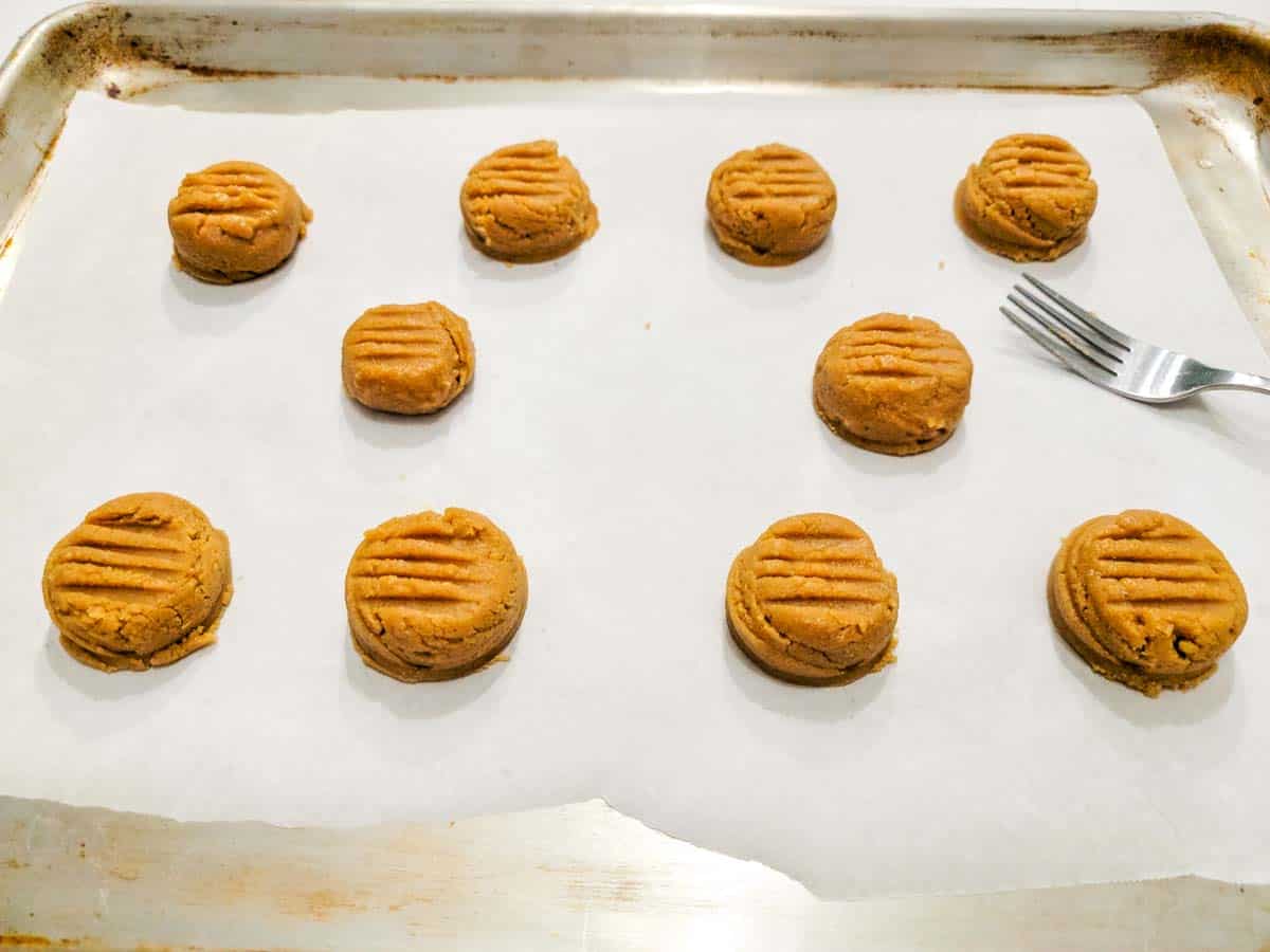 Peanut Butter Cookies pressed with fork tines on a cookie sheet.