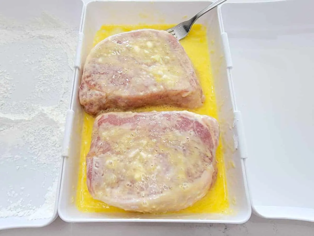 two boneless pork chops coated in beaten egg.
