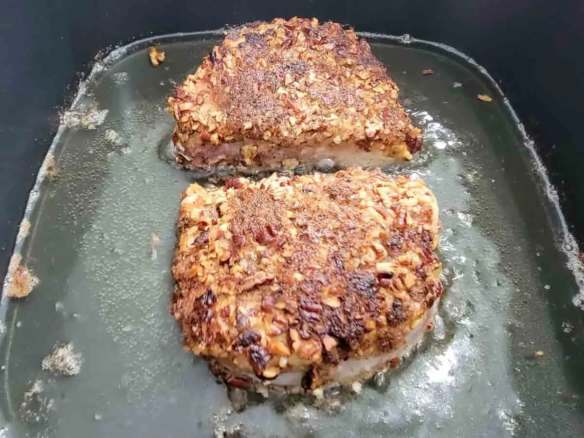 two boneless pecan crusted pork chops frying in oil.