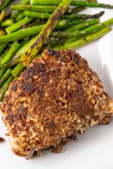 a Pecan Crusted Pork Chop with a side of asparagus on a plate.