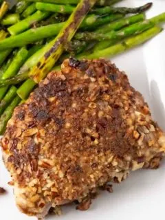 a Pecan Crusted Pork Chop with a side of asparagus on a plate.