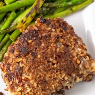 a Pecan Crusted Pork Chop with a side of asparagus on a plate.