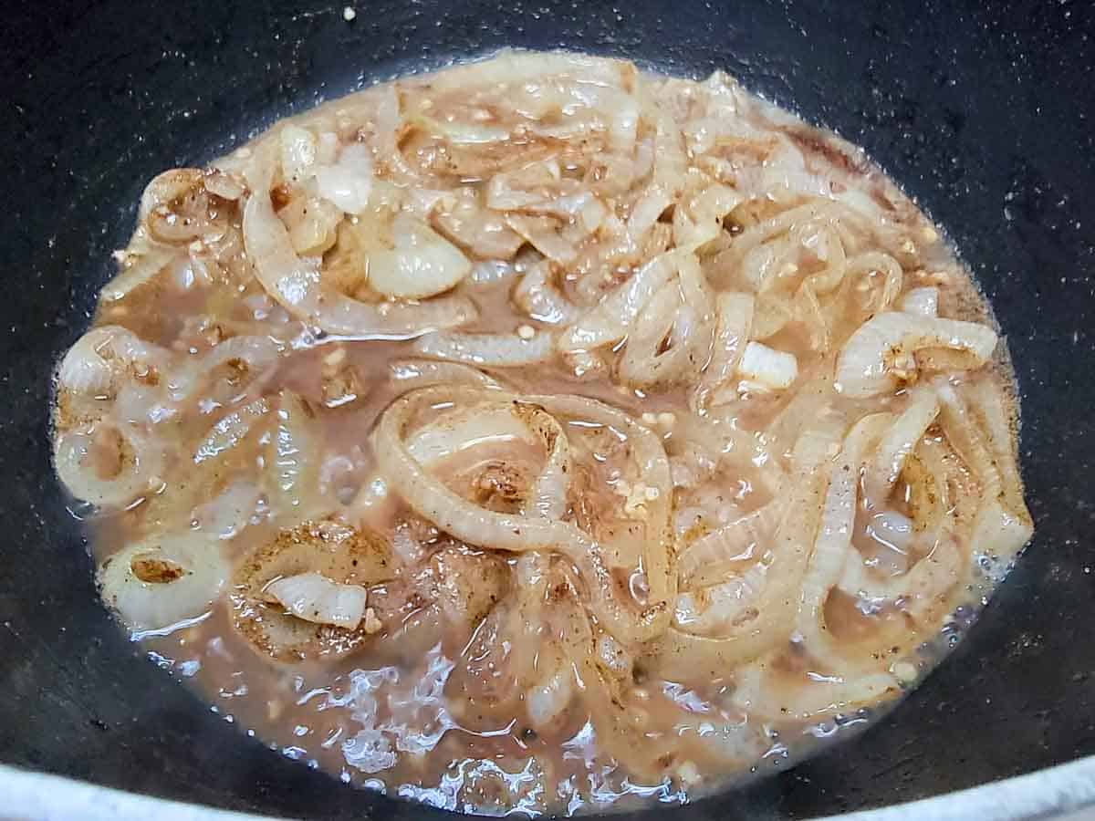 onions, seasonings, and chicken stock cooking in a pan.