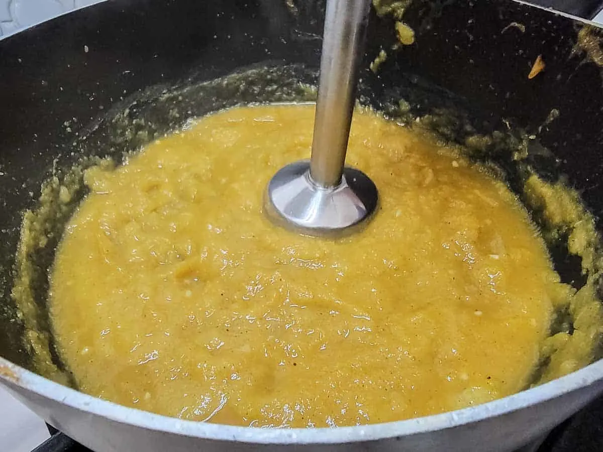 a handheld immersion blender blending pumpkin soup in a pan.