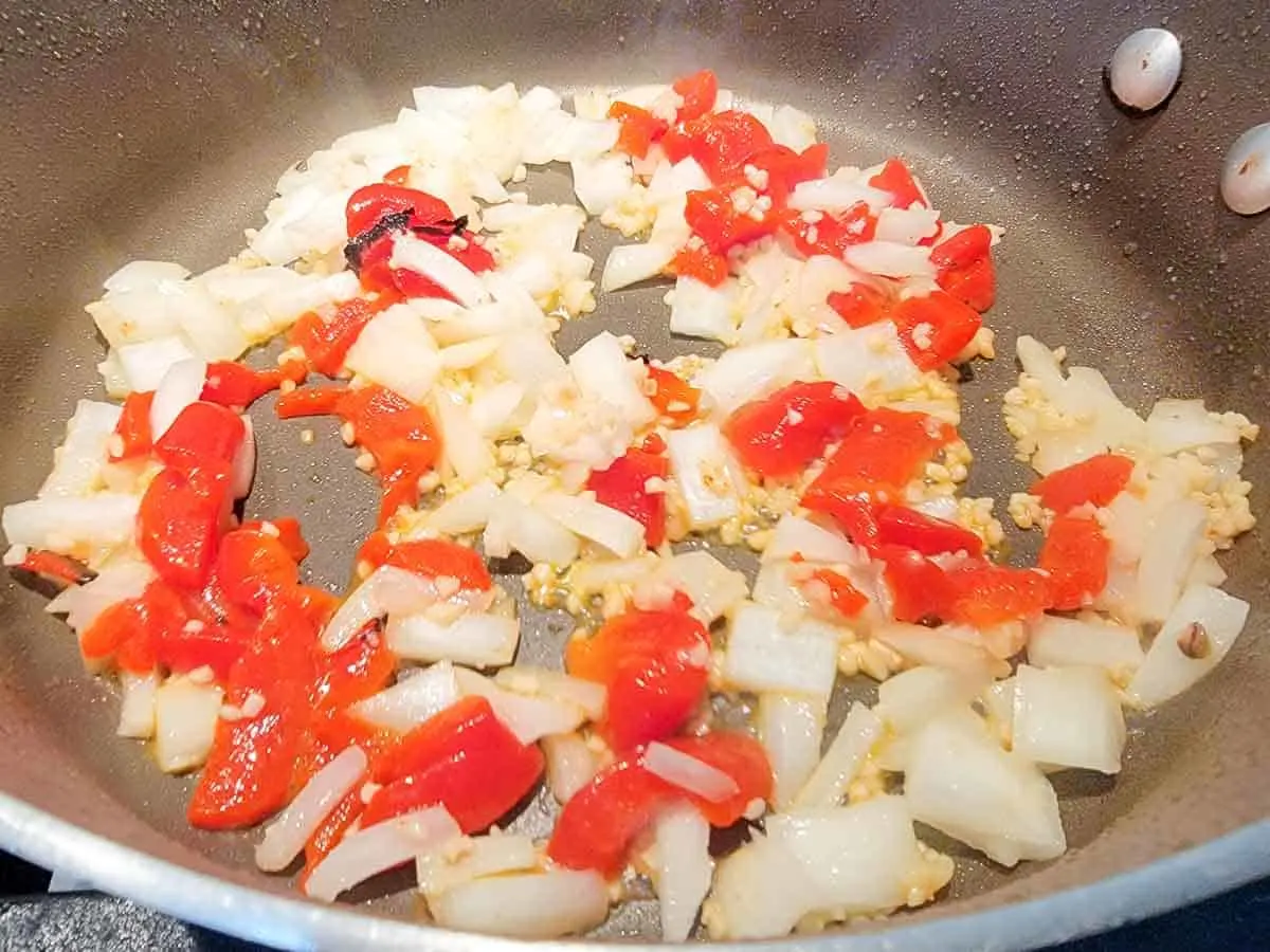 onions, red peppers and garlic cooking in a pan.