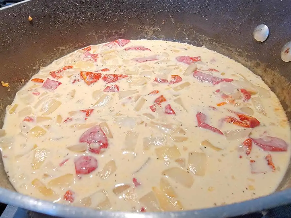 creamy garlic sauce with onions and red peppers in a pan.