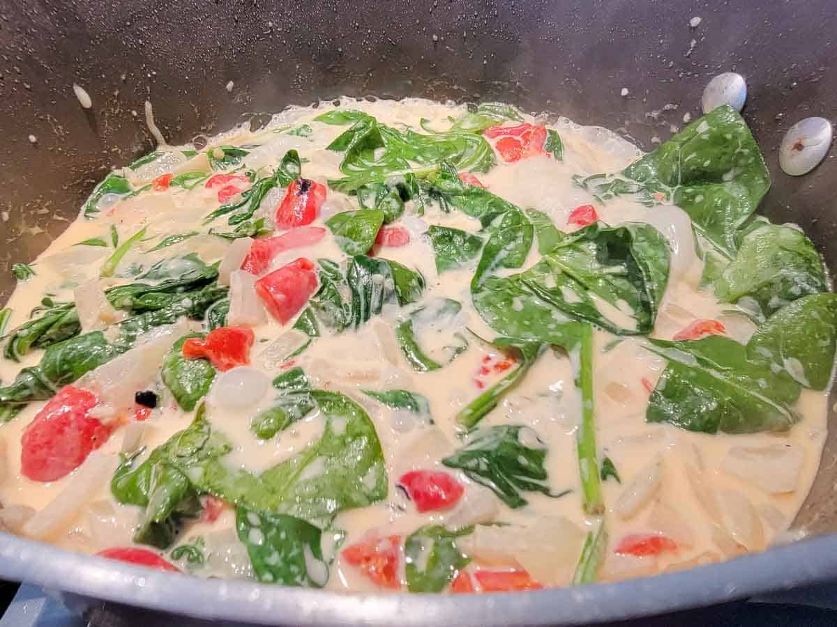 creamy garlic sauce with spinach, onions and red peppers in a pan.