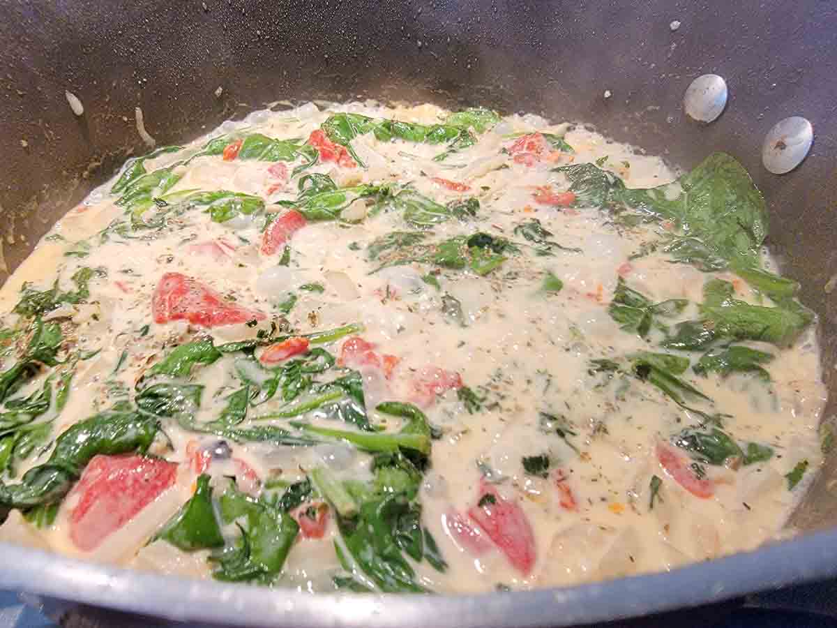 creamy garlic sauce with spinach, seasonings, onions and red peppers in a pan.
