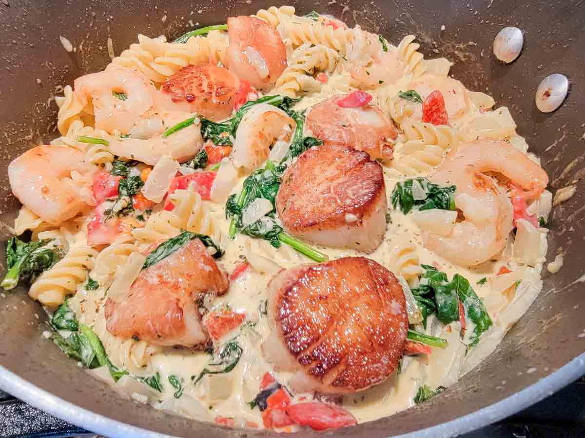 shrimp and scallop pasta cooking in a pan.