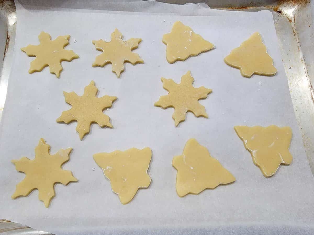 10 snow flake and christmas tree shaped unbaked sugar cookies on a cookie sheet.
