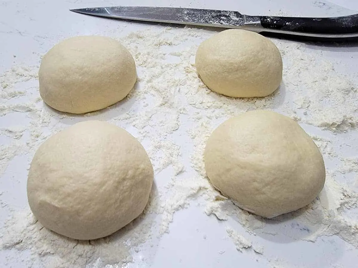 4 flatbread dough balls on a floured surface.