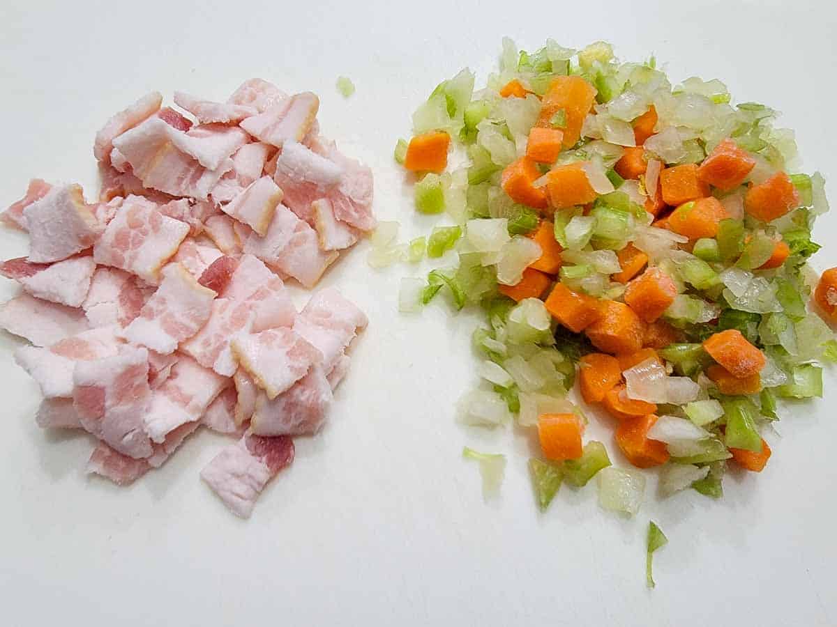 diced bacon, celery, onion, and carrot on a cutting board.