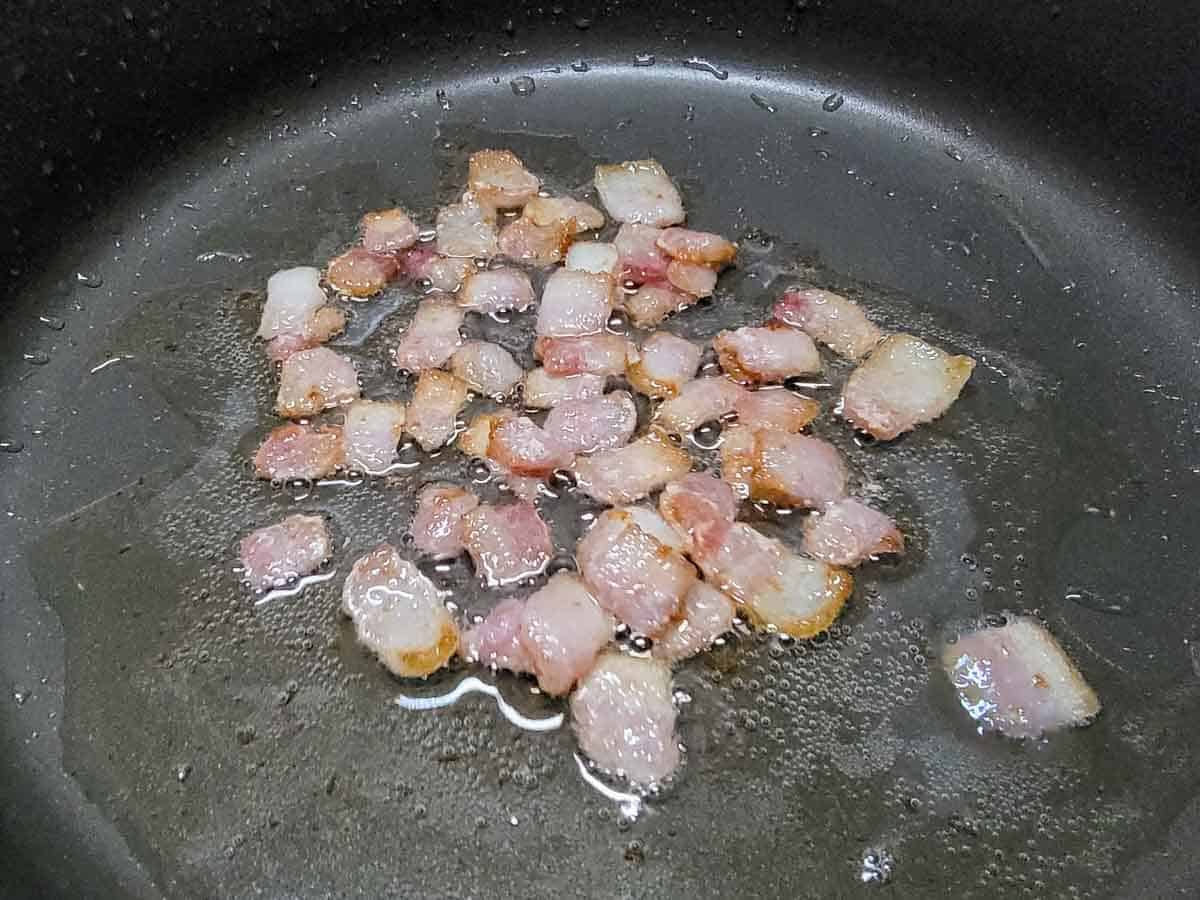 diced bacon frying in a pan.