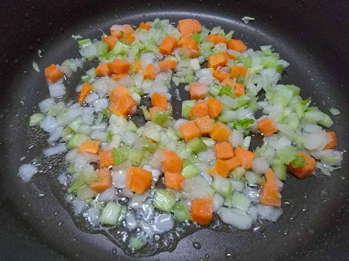 diced onion, celery, and carrots frying in a pan.