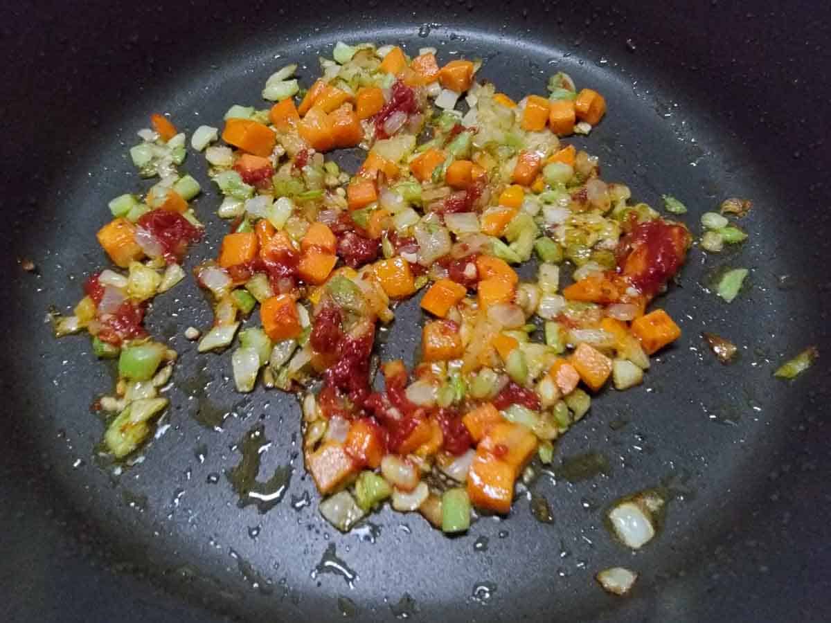 diced onion, celery, minced garlic, tomato paste, and carrots frying in a pan.