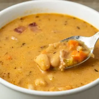 a bowl filled with Bean and Bacon Soup and a spoon lifting some out.