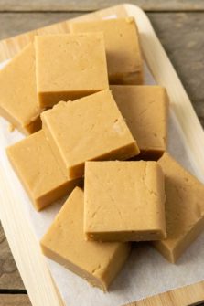 Peanut Butter Fudge squares stacked in a pile on parchment paper.