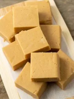 Peanut Butter Fudge squares stacked in a pile on parchment paper.