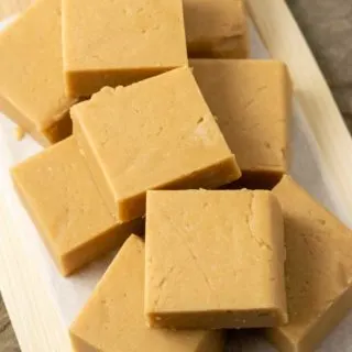 Peanut Butter Fudge squares stacked in a pile on parchment paper.